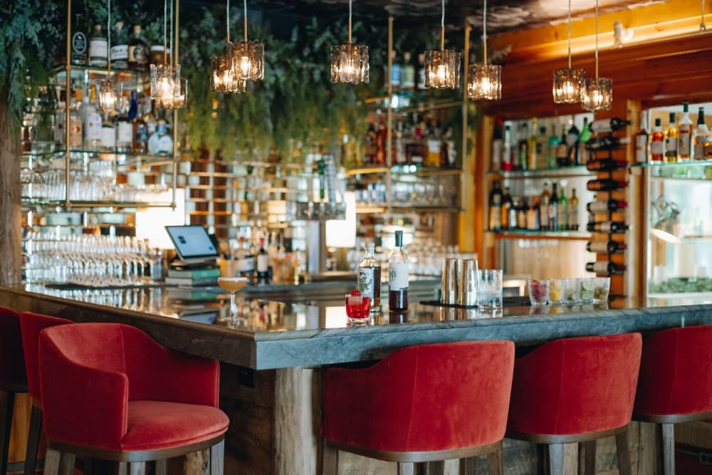 A stylish bar with red chairs, a marble countertop, and shelves stocked with various bottles of alcohol.