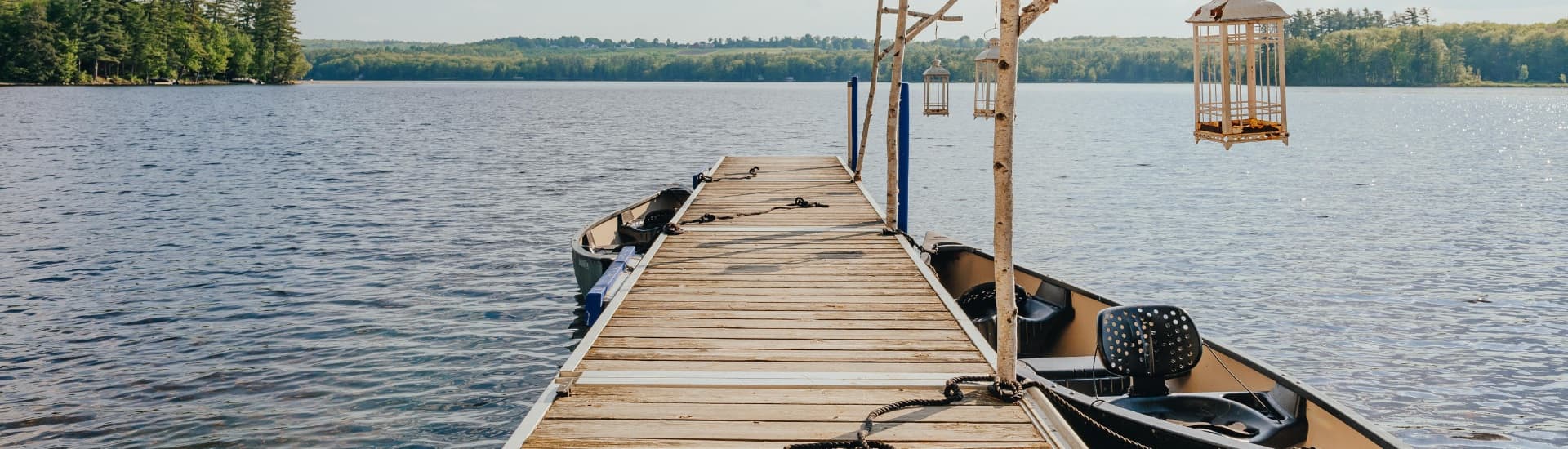 A wooden dock extends over a calm lake, featuring boats and hanging lanterns.