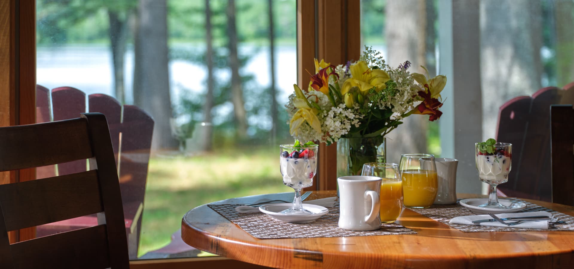 A beautifully set breakfast table featuring parfaits, juice, and a vase of flowers, with a serene outdoor view.