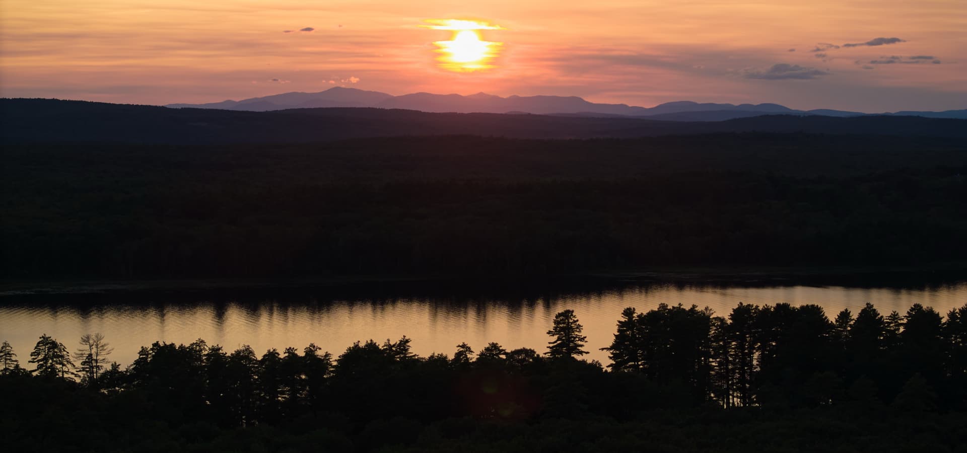 A vibrant sunset over a calm lake surrounded by mountains and trees.