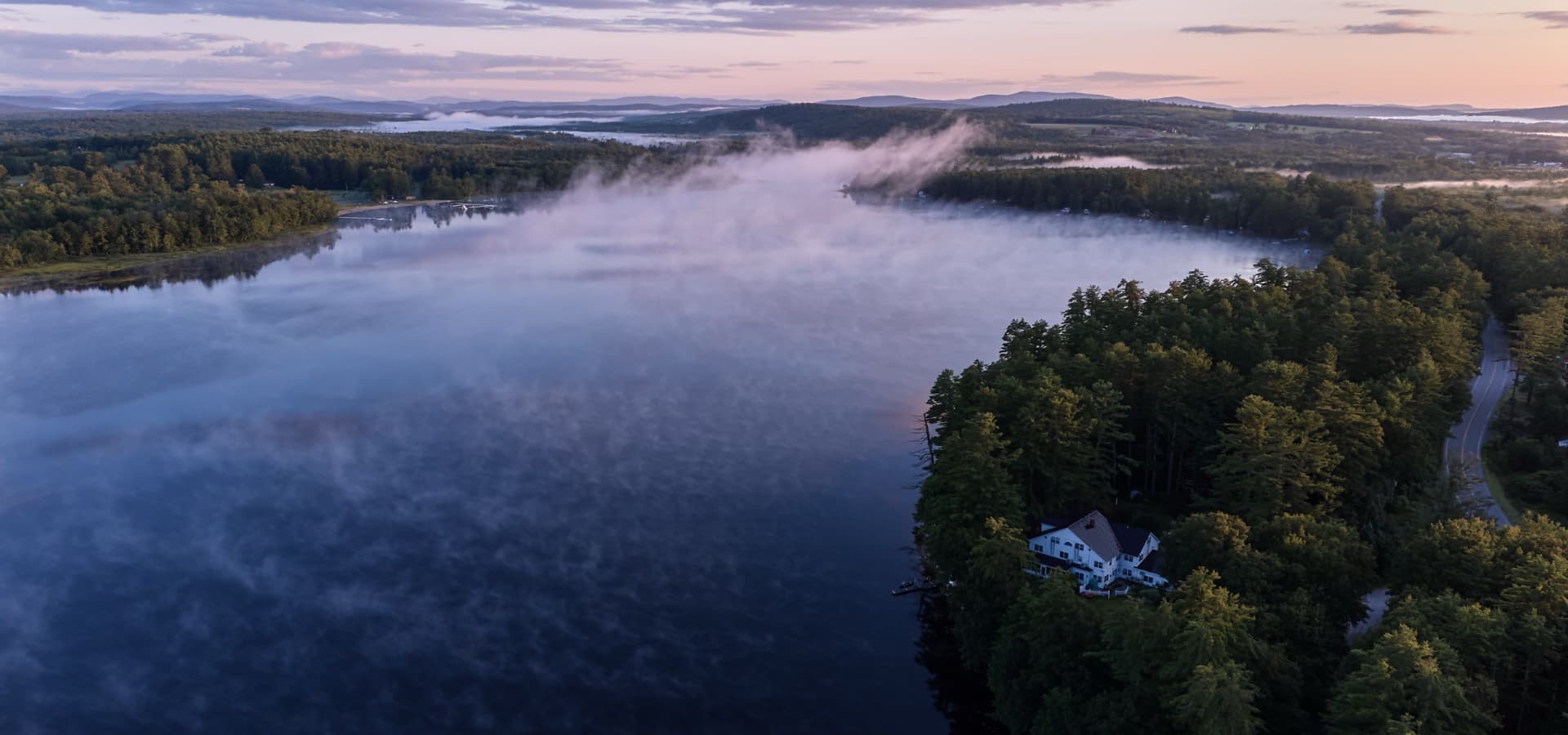 A scenic aerial view of a misty lake surrounded by lush forests at sunrise.