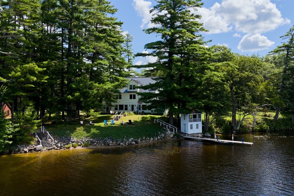 A serene lakeside property surrounded by tall trees, featuring a white house and a small dock.