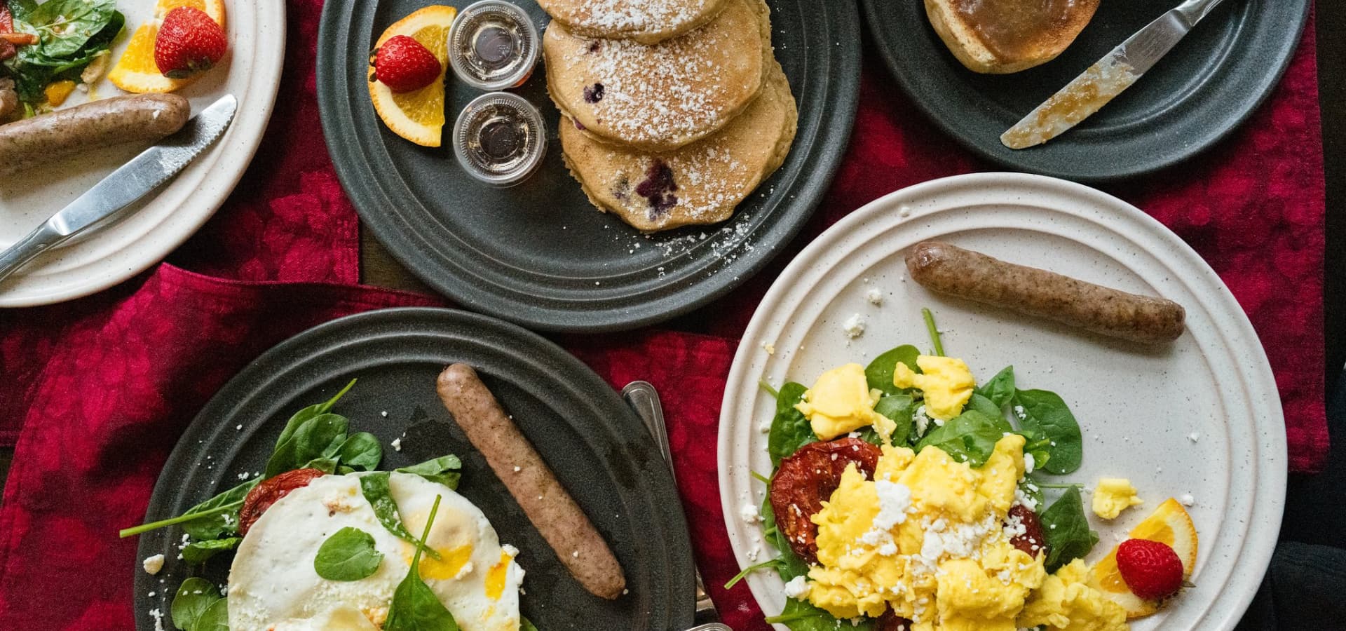 A breakfast spread featuring pancakes, sausage, scrambled eggs on spinach, and fresh strawberries.