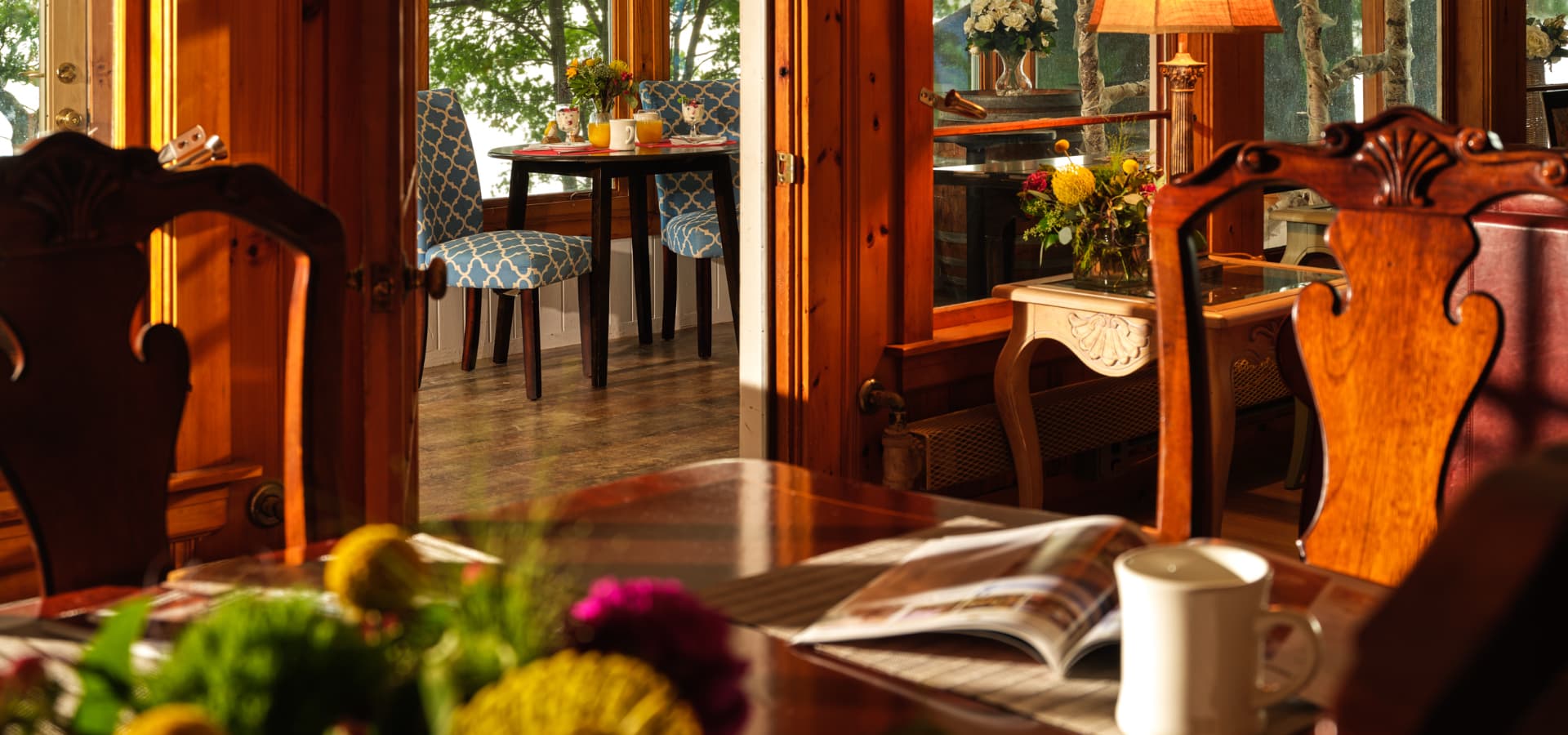 A warm, inviting dining area with wooden furnishings and blue-patterned chairs, illuminated by natural light.