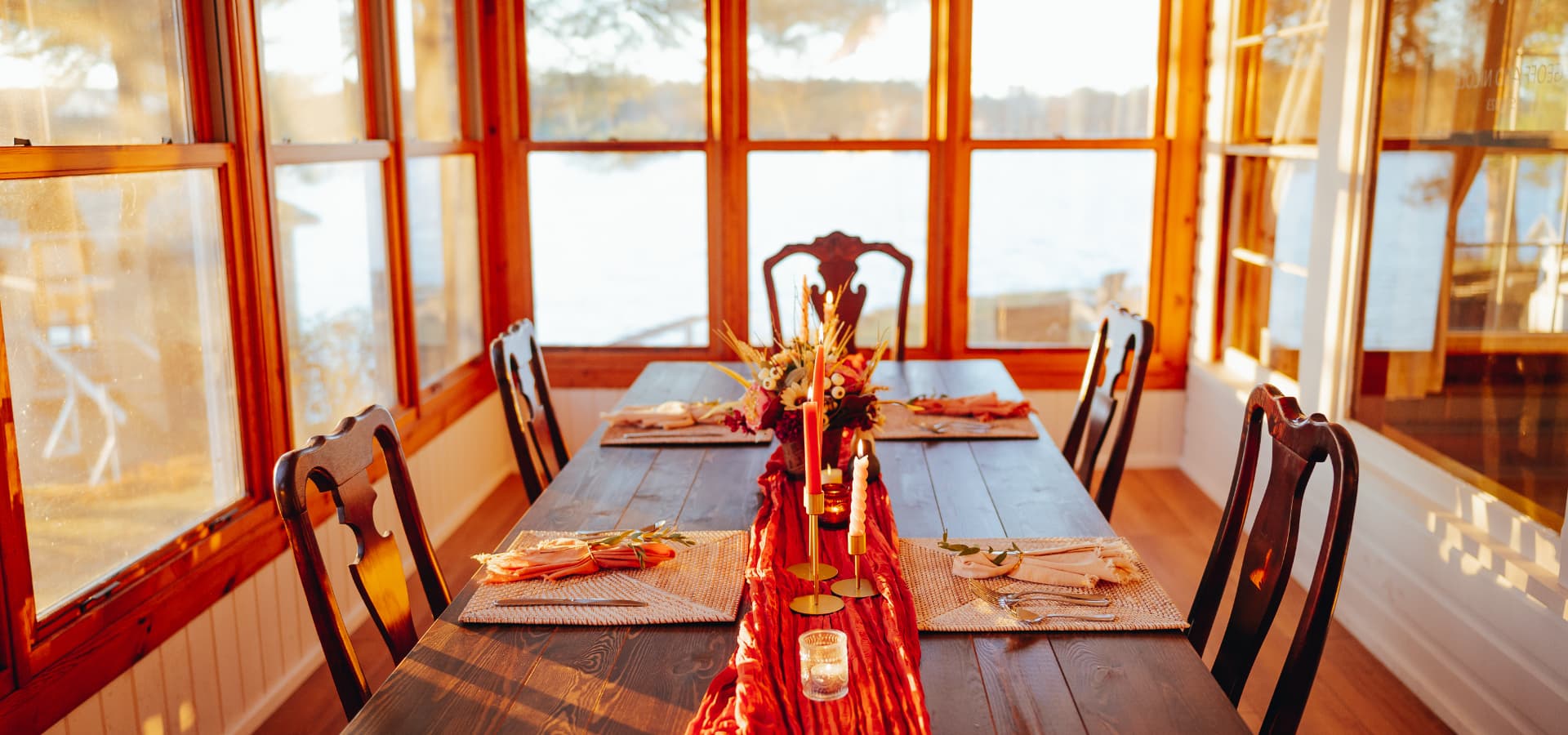 A beautifully set dining table with a floral centerpiece, surrounded by large windows and soft evening light.