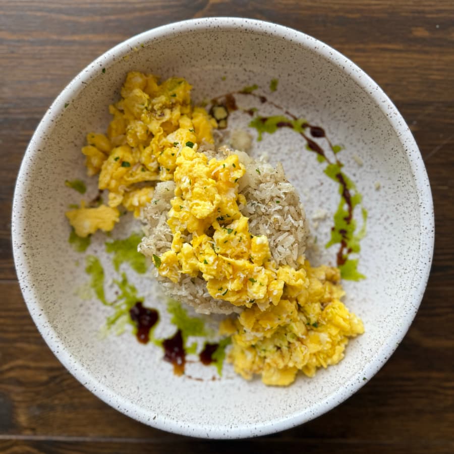 A bowl of fluffy scrambled eggs on a bed of rice, drizzled with green and dark sauces.