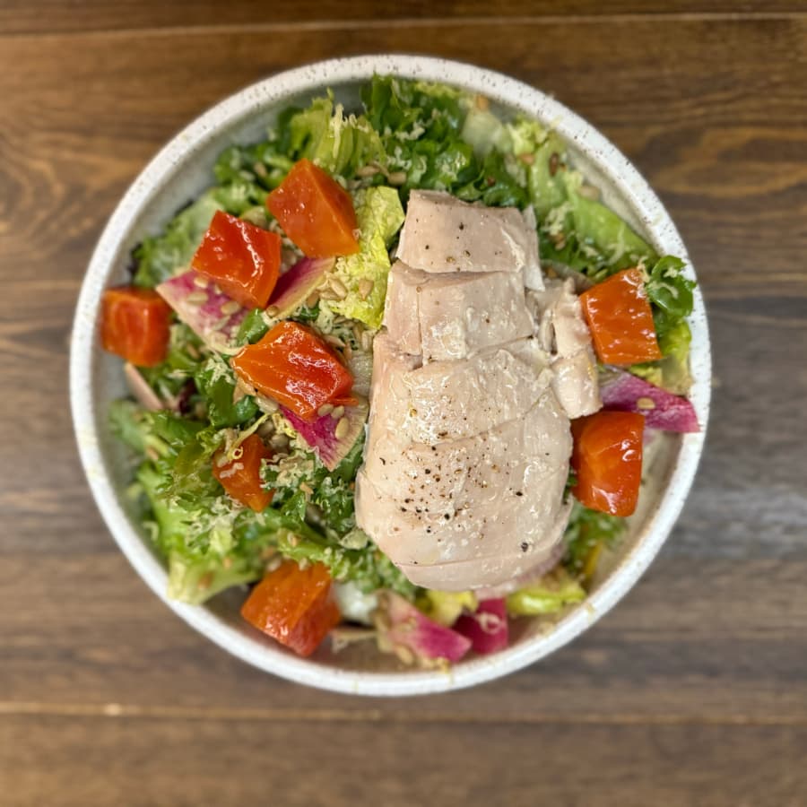 A bowl of mixed greens topped with slices of grilled chicken and chunks of roasted red peppers.